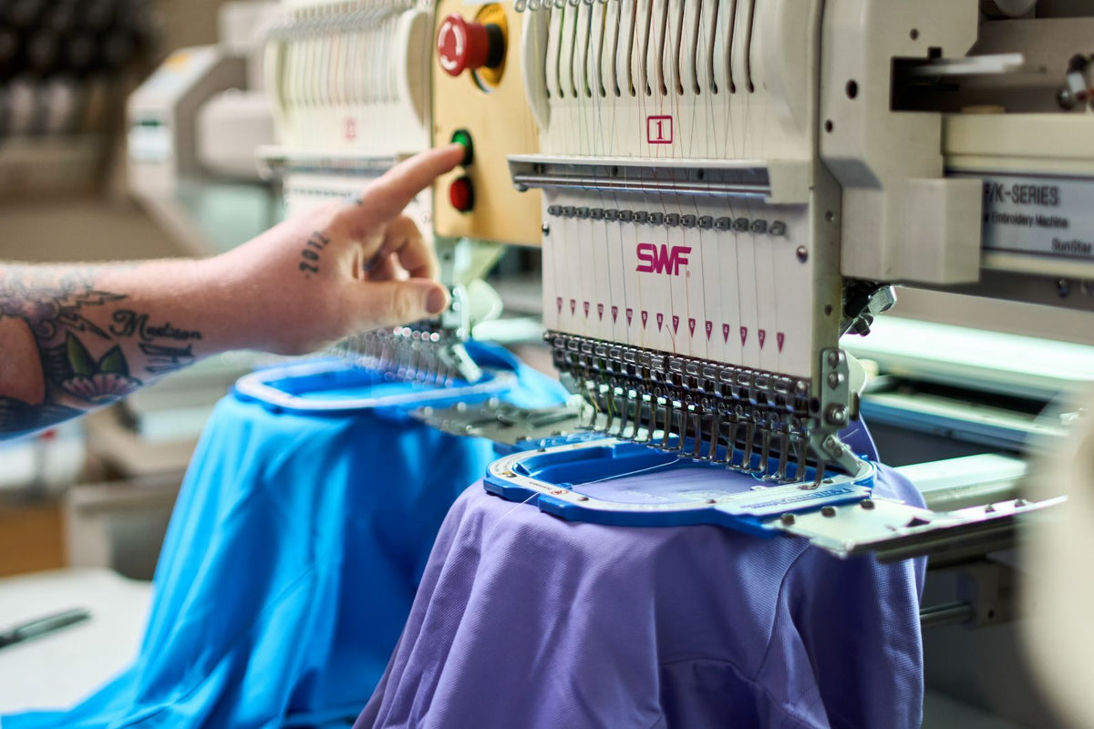 Person operating an embroidery machine with a tattooed arm, focusing on the machine's control panel.